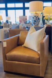 Tan leather armchair with a white pillow, surrounded by modern decor and warm lighting in a stylish interior design boutique